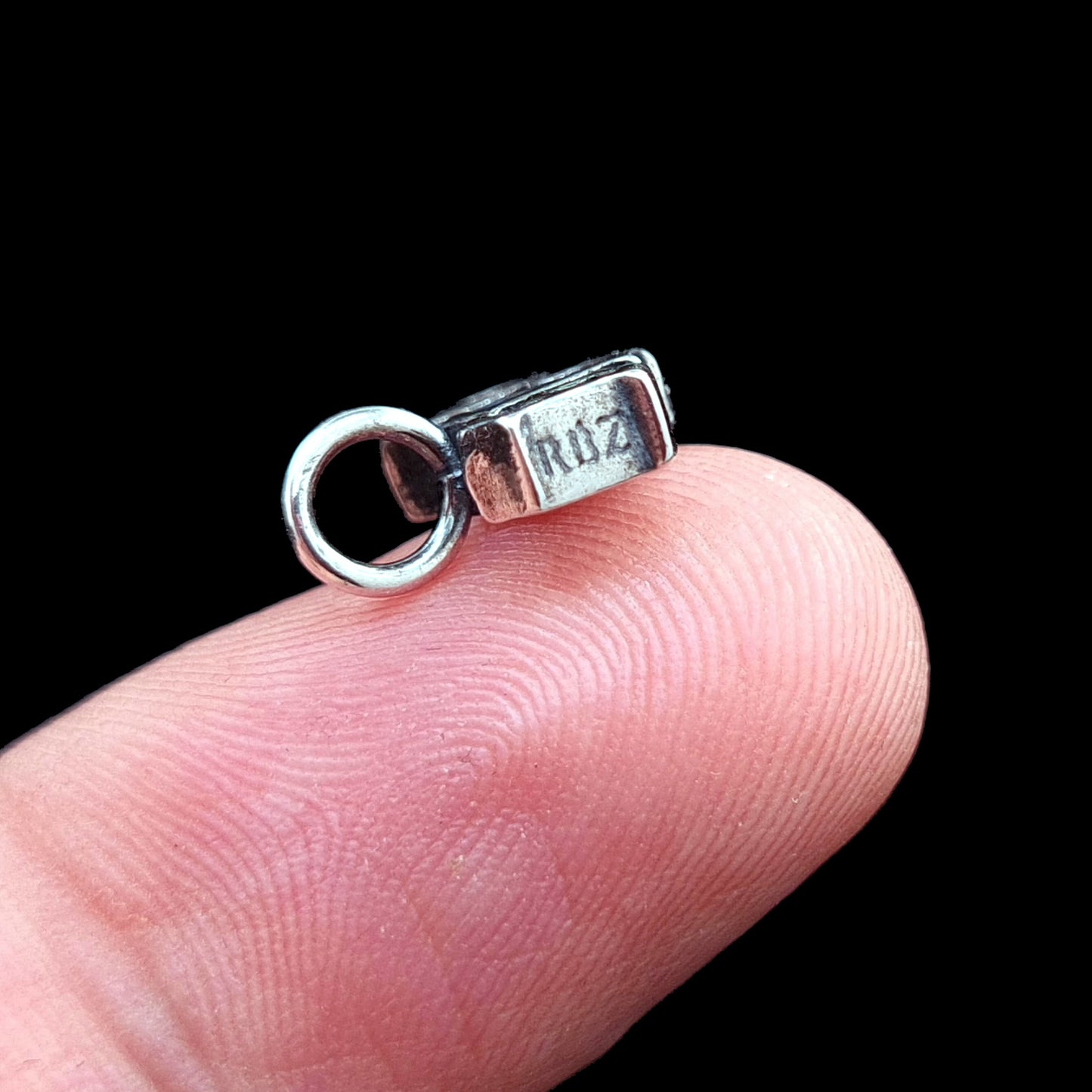 Side view of the dainty Sterling silver 666 pendant by RBZ Jewelry held on a finger for scale, showcasing the RBZ logo engraving on the side and the oxidized finish of the Gothic-font numbers.