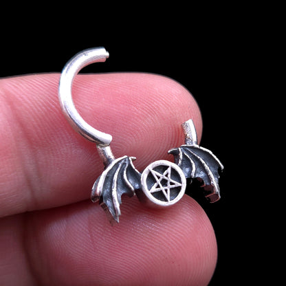 Gothic 925 sterling silver winged pentagram septum clicker ring by RBZ Jewelry, held open between two fingers against a black background to demonstrate the hinged clicker mechanism and size proportions.
