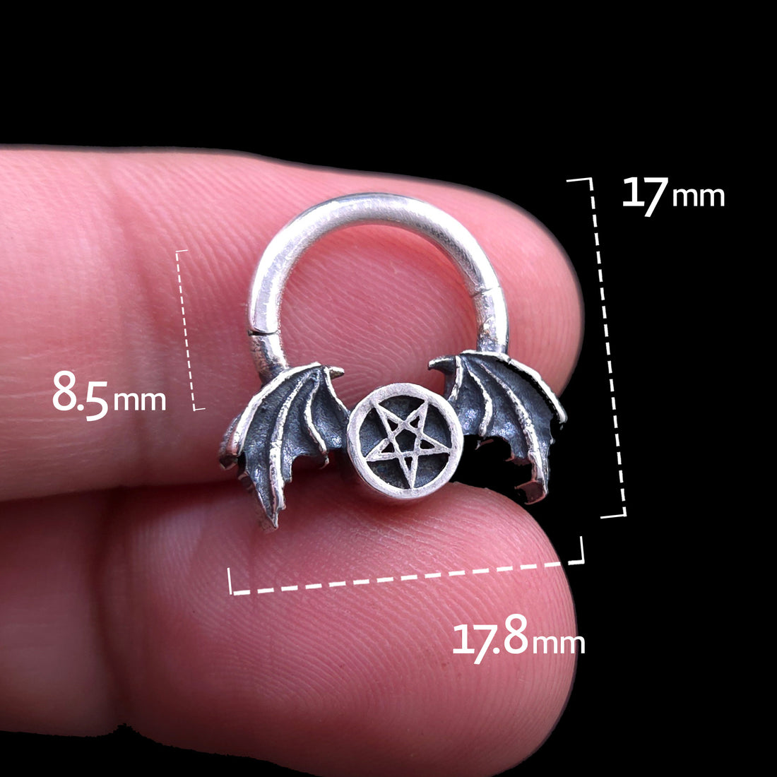 Front view of the gothic 925 sterling silver winged pentagram septum clicker ring by RBZ Jewelry held between two fingers, featuring graphic dimension lines showing measurements of 17.8mm total width, 17mm total height, and 8.5mm inner drop.