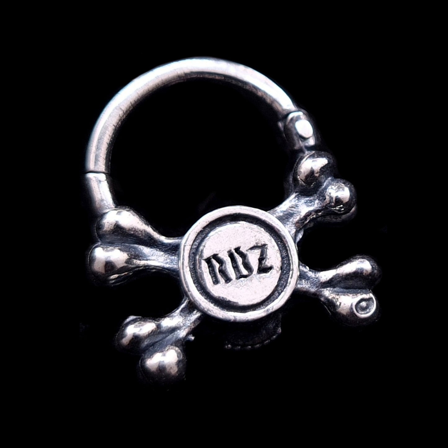 Back view of the sterling silver crossbones septum ring by RBZ Jewelry, showcasing the official RBZ maker's mark engraved in a gothic font on the reverse of the oxidized skull.