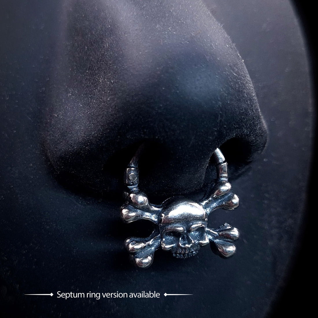 Sterling silver crossbones skull septum ring by RBZ Jewelry, displayed worn on a life-size black silicone nose to demonstrate fit and the bold, oxidized gothic memento mori design.