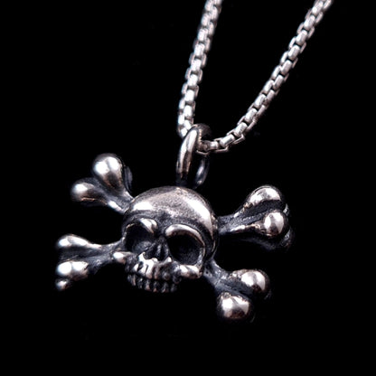 Handcrafted Gothic sterling silver skull and crossbones pendant by RBZ Jewelry, featuring intricate oxidized detailing and a polished finish, hanging from a silver box chain against a black background.