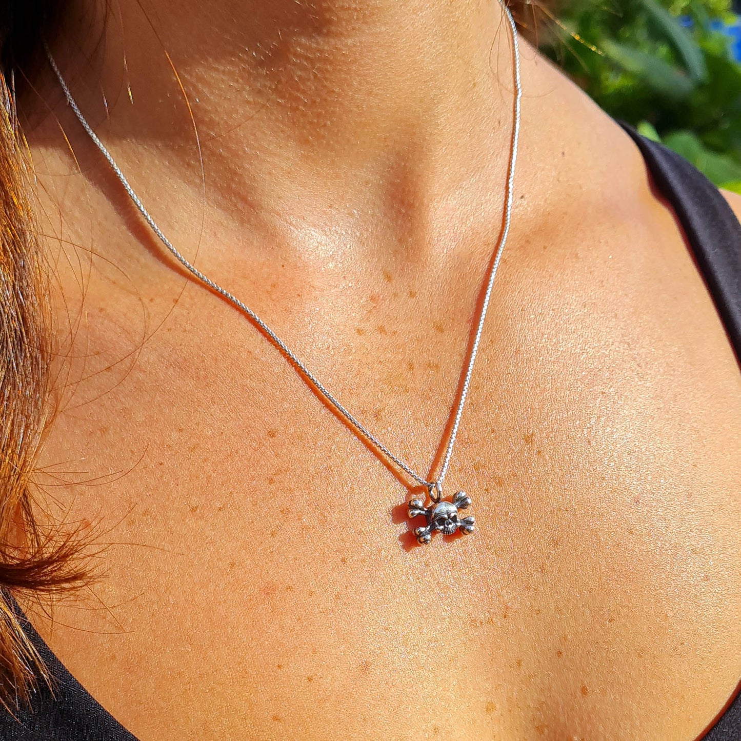 Lifestyle view of a female model wearing the RBZ Jewelry sterling silver skull and crossbones pendant, illustrating its dainty scale and subtle Gothic aesthetic on a polished silver chain.