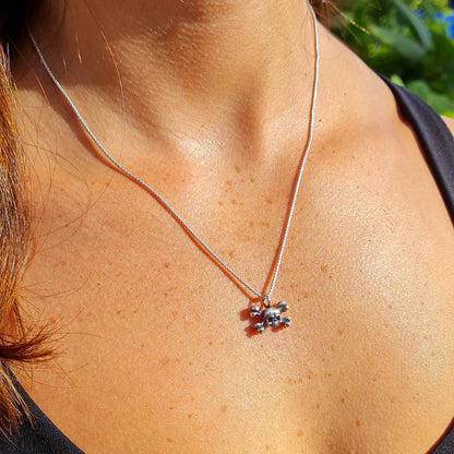 Lifestyle view of a female model wearing the RBZ Jewelry sterling silver skull and crossbones pendant, illustrating its dainty scale and subtle Gothic aesthetic on a polished silver chain.