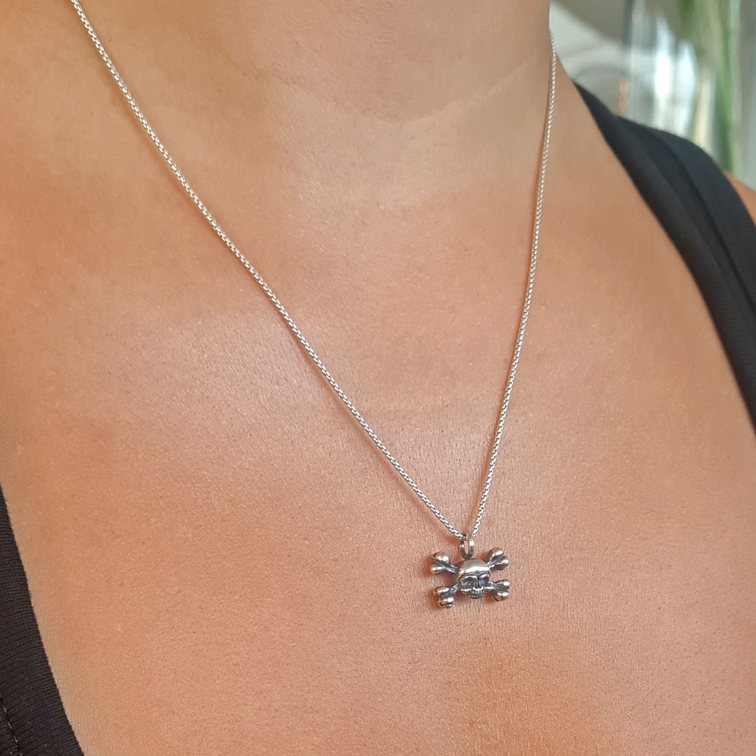 Lifestyle view of a female model wearing the RBZ Jewelry dainty sterling silver skull and crossbones pendant on a fine silver chain, highlighting its subtle scale and intricate Gothic craftsmanship.