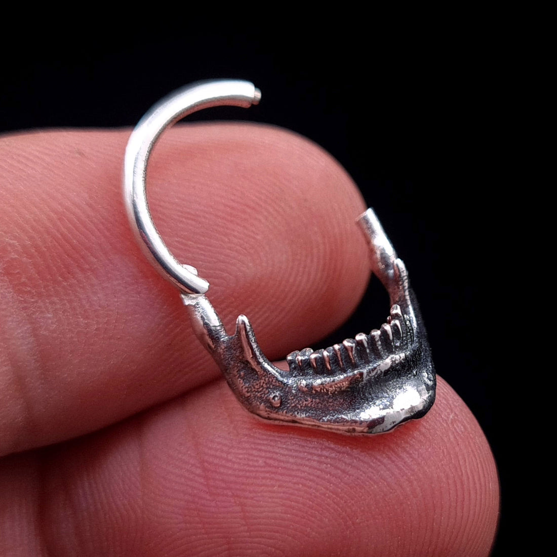 Sterling silver Reaped Mandible septum ring by RBZ Jewelry held in hand to show scale, featuring the gothic anatomical jaw design and the clicker mechanism in the open position.