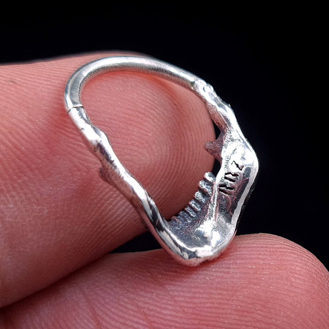 Back view of the Sterling silver Reaped Mandible clicker septum ring by RBZ Jewelry held in hand for scale, highlighting the detailed anatomical jaw and the signature RBZ logo engraving on the interior.