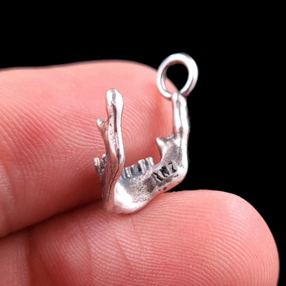 Handcrafted sterling silver skull jaw pendant by RBZ Jewelry held on a fingertip for scale, showing the rear view with the engraved RBZ logo on the inner mandible. The detailed gothic skeletal texture and oxidized finish of the Memento Mori charm are clearly visible against a black background.