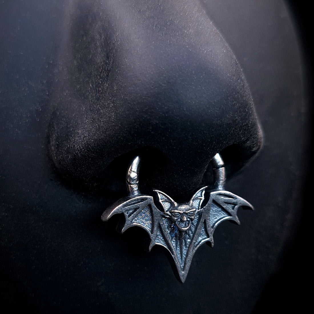 Sterling silver Gothic vampire bat septum clicker ring by RBZ Jewelry, displayed on a life-size black silicone nose model to showcase the fit and detailed oxidized silver finish.