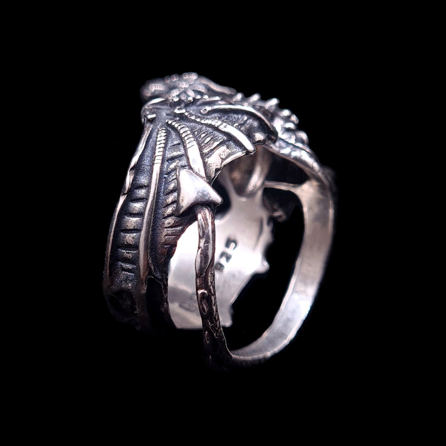 Gothic sterling silver dragon ring by RBZ Jewelry, showing the interior band stamped with a 925 hallmark, detailed webbed wings, and the sharp spade tip of the interlocking wrapped tail against a black background.
