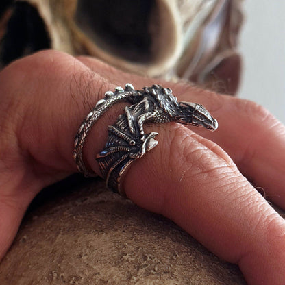 Gothic sterling silver dragon ring by RBZ Jewelry, worn on a male model's finger, showcasing the detailed webbed wings, heavily oxidized textured scales, and the interlocking wrapped tail band.