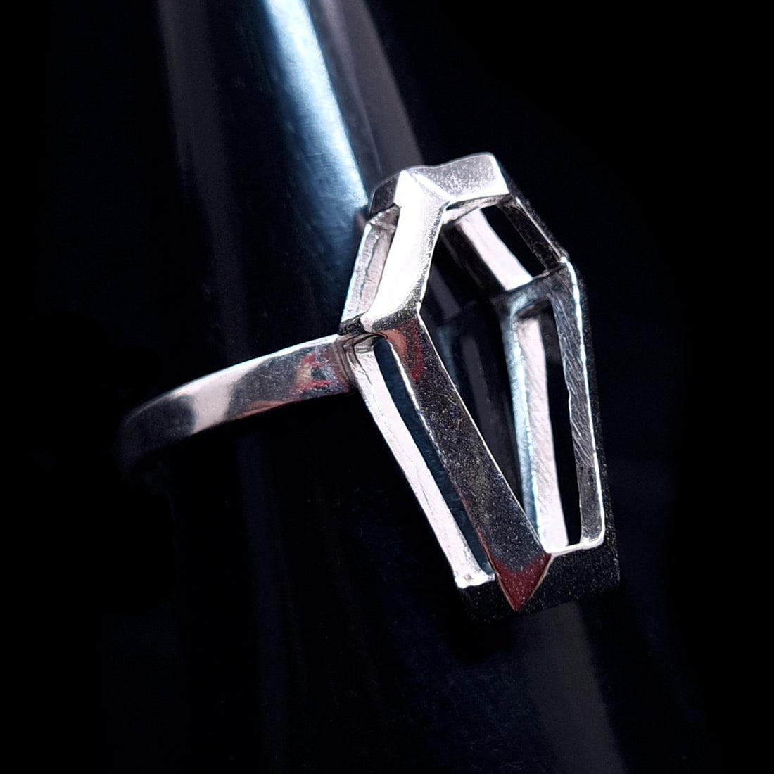 RBZ Jewelry Sterling Silver Minimalist Coffin Ring with hollow architectural frame and intricate geometric design facing right on a dark mandrel. The skeletal coffin-shaped setting is open to create light and shadow effects.