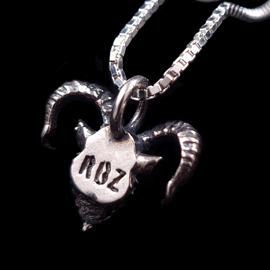 RBZ Jewelry Gothic Sterling Horned Demon pendant back view: The reverse side of the oxidized sterling silver demon head featuring the RBZ brand hallmark stamp, shown on a silver box chain against a solid black background.