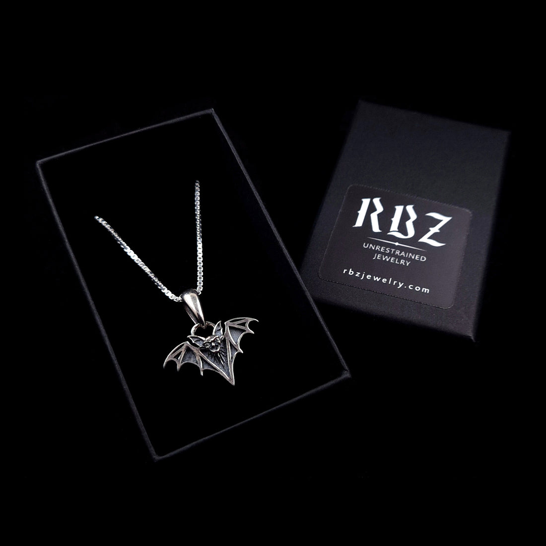 Gothic Sterling silver vampire bat necklace featuring an intricate fanged face and skeletal wings with deep black oxidation and polished silver highlights, displayed in a black box with the RBZ brand logo and website address.