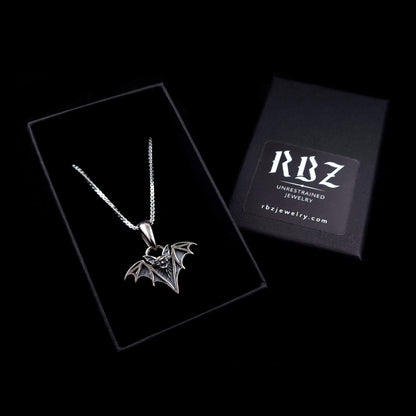 Gothic Sterling silver vampire bat necklace featuring an intricate fanged face and skeletal wings with deep black oxidation and polished silver highlights, displayed in a black box with the RBZ brand logo and website address.