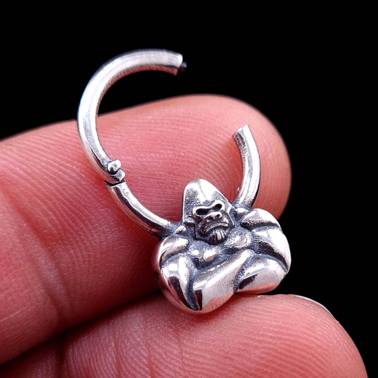 Sterling silver Jungle Gorilla septum clicker ring by RBZ Jewelry held between fingers, showing the hinged mechanism in the open position to highlight the ease of wear and the detailed gorilla bust design.