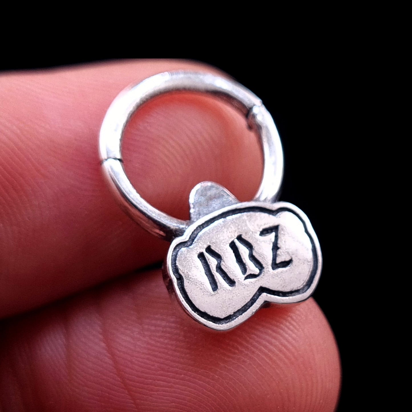 Close-up of the back of the sterling silver Jungle Gorilla septum clicker ring by RBZ Jewelry held between fingers, showcasing the engraved RBZ logo and providing a sense of scale for the detailed jewelry piece.
