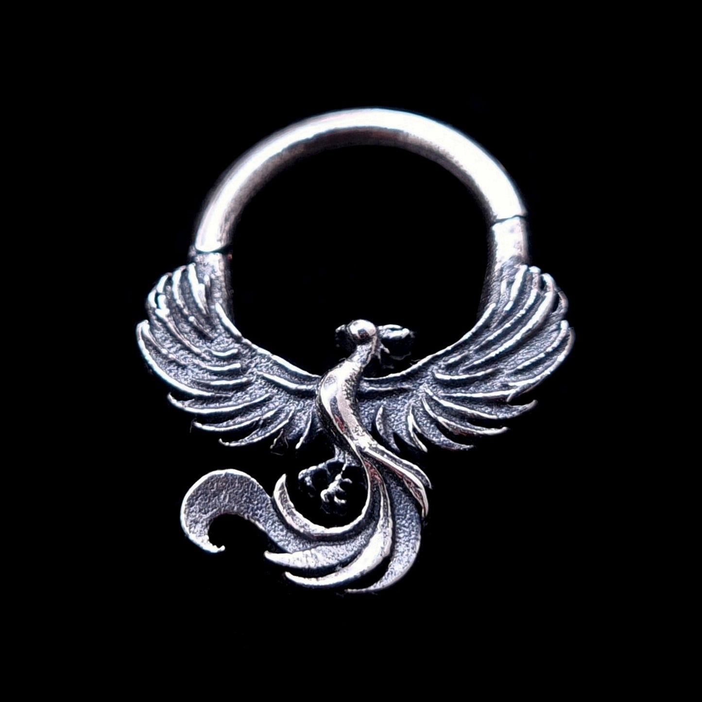 Detailed sterling silver Soaring Phoenix septum clicker ring by RBZ Jewelry, featuring an intricately carved phoenix with outstretched wings and a curved tail, captured in a moment of ascent against a solid black background.