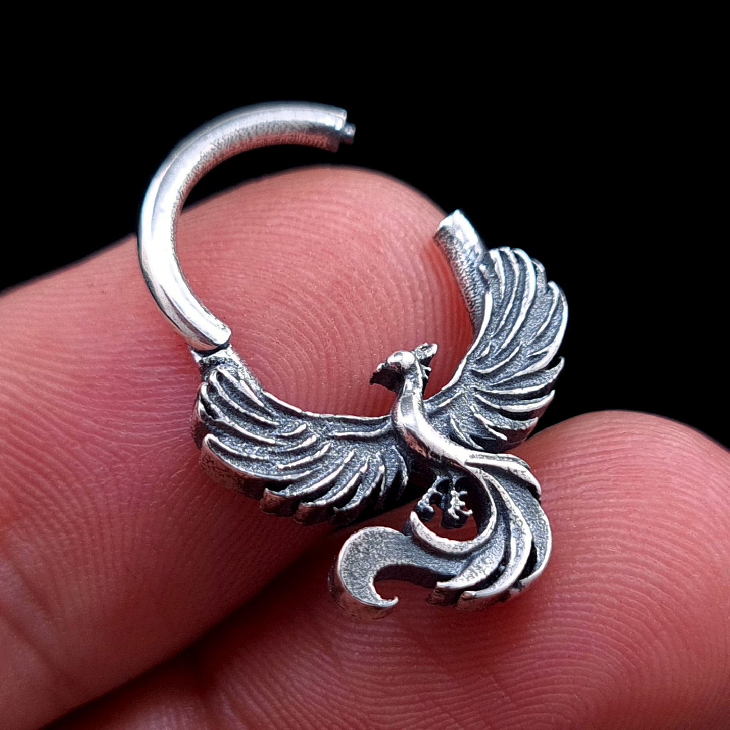 Sterling silver Soaring Phoenix septum ring by RBZ Jewelry held in hand with the clicker hinge open, illustrating the scale and functional design of the intricately detailed phoenix body jewelry.