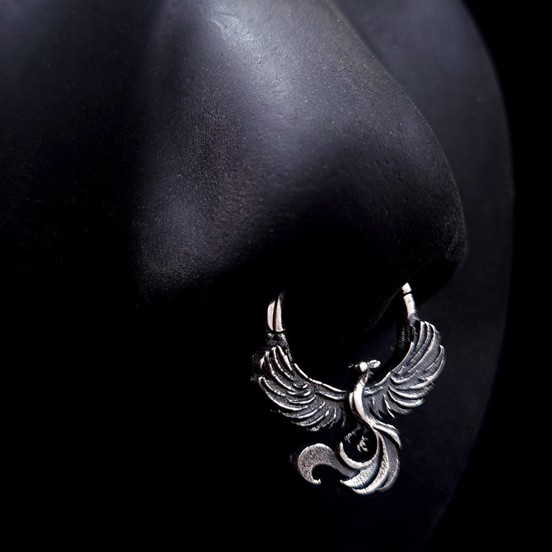 Sterling silver Soaring Phoenix septum ring by RBZ Jewelry displayed on a life-size black silicone nose mannequin, showcasing the anatomical fit and the bold, unrestrained aesthetic of the intricately carved phoenix design.
