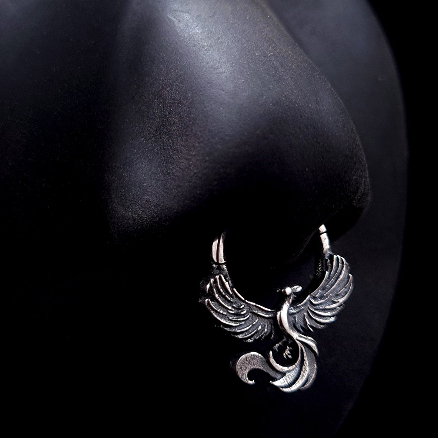 Sterling silver Soaring Phoenix septum ring by RBZ Jewelry displayed on a life-size black silicone nose mannequin, showcasing the anatomical fit and the bold, unrestrained aesthetic of the intricately carved phoenix design.