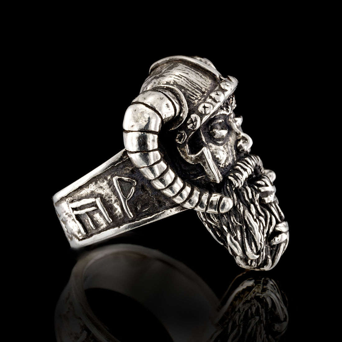 A macro view of the left-hand side profile of the RBZ Jewelry Sterling silver Viking Warrior ring. This detailed perspective focuses on the intricate outer shank band, which prominently displays a sequence of four hand-sculpted runic inscriptions, including the Axe-Hammer (Mjöllnir), and specific symbols for Joy, Wealth, and Giving, as described in the product details. The detailed left-side profile of the weathered warrior’s face and beard is also clearly visible. The aged silver ring rests on a black BG.