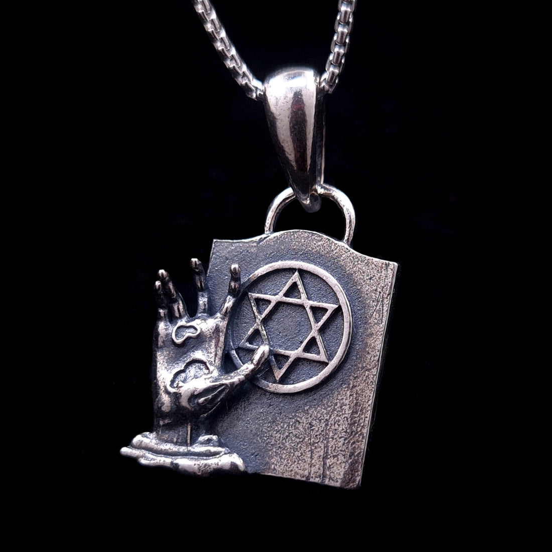Sterling silver Gothic Star of David pendant featuring a detailed decaying zombie hand emerging from the ground next to a weathered tombstone. This macabre Judaica statement piece blends horror aesthetics with the concept of Techiyat HaMetim (resurrection of the dead), created by RBZ Jewelry.