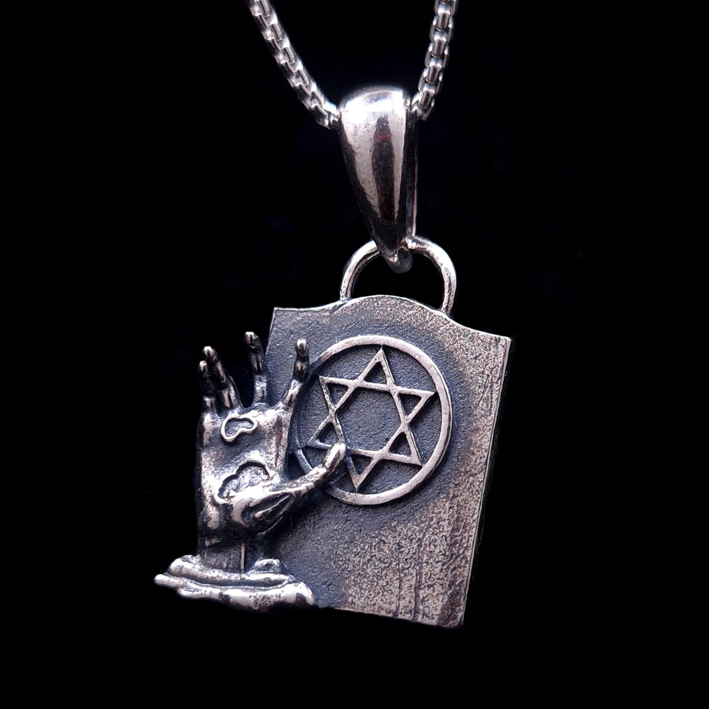 Sterling silver Gothic Star of David pendant featuring a detailed decaying zombie hand emerging from the ground next to a weathered tombstone. This macabre Judaica statement piece blends horror aesthetics with the concept of Techiyat HaMetim (resurrection of the dead), created by RBZ Jewelry.